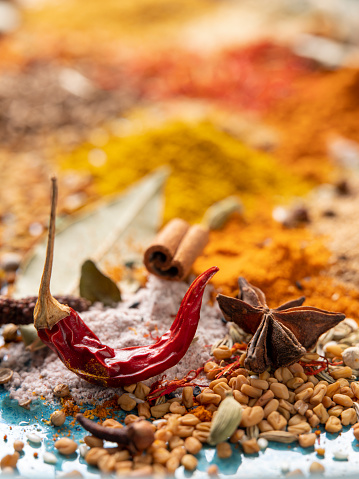 Many colorful, organic, dried, vibrant Indian food, ingredient spices are displayed on an old turquoise-colored ceramic plate background.
