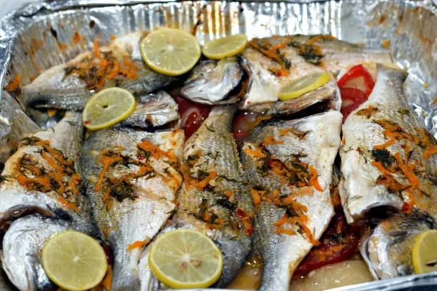 Photo of Seafood cuisine, sea bream fishes cooked in the oven with lime slices, tomatoes and onion rings in a foil plate, gilt-head bream fishes recipe, denise fish cooked, selective focus