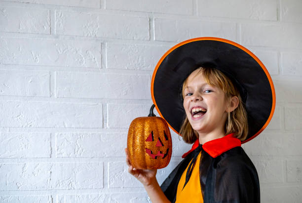 dziecko ubrane w kostium czarownicy trzyma w rękach ozdobną dynię. zło się śmieje. koncepcja obchodów halloween - house halloween autumn candid zdjęcia i obrazy z banku zdjęć