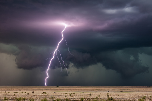 A bright lightning bolt strike from a thunderstorm with dramatic storm clouds during a severe weather event near House, New Mexico.