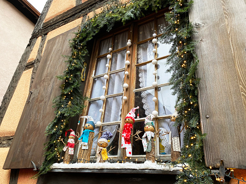 Stylish Christmas decorations on window sill, christmas tree and fir branches with christmas ornaments on street in Colmar