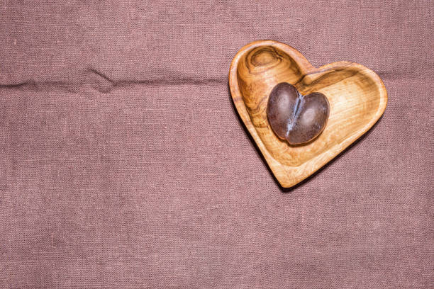 Ripe brown and blue natural malformed imperfect plum with crack in middle on wooden heart shaped plate on lilac linen material with fold in shape of cardiogram. Large copy space. Directly above view