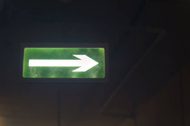istock Illuminated green exit sign suspended from the ceiling in a public building. 1351616468