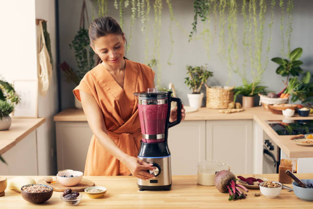 Young female pressing start button of blender while cooking