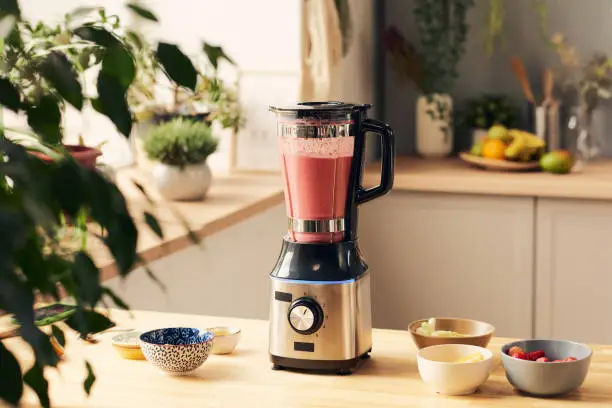 Photo of Electric blender with fresh homemade fruit smoothie on table