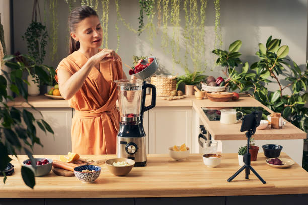 istock Young female blogger putting strawberries into blender 1351622016