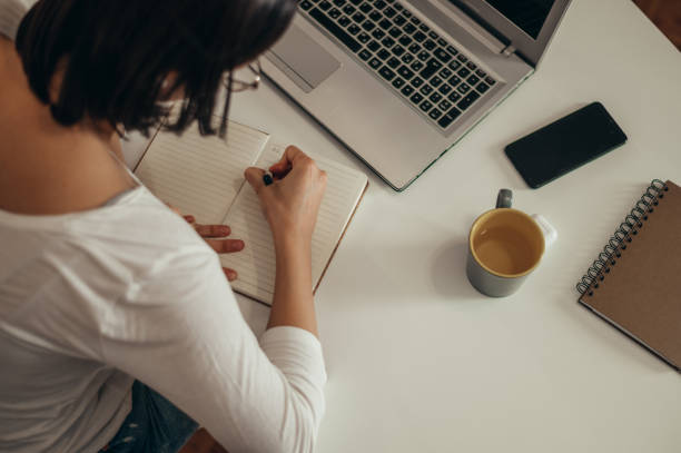 istock Woman writing in a notebook and using a laptop while working from home 1351623252