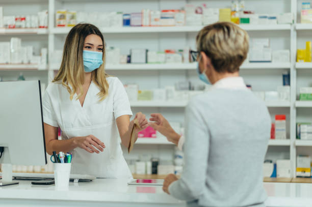 farmaceuta noszący maskę ochronną i obsługujący pacjenta klienta w aptece - pharmacist mature adult smiling senior adult zdjęcia i obrazy z banku zdjęć