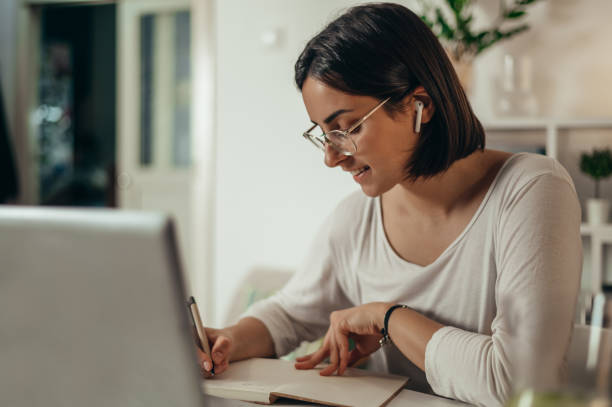 istock Woman writing in a notebook and using a laptop while working from home 1351623891