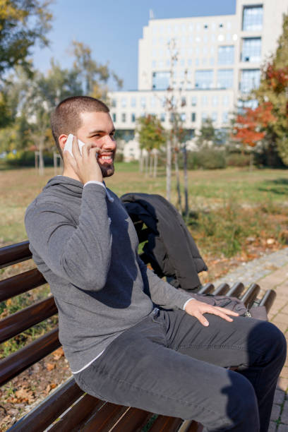 istock Young man sitting on a park bench and having a phone conversation 1351627958