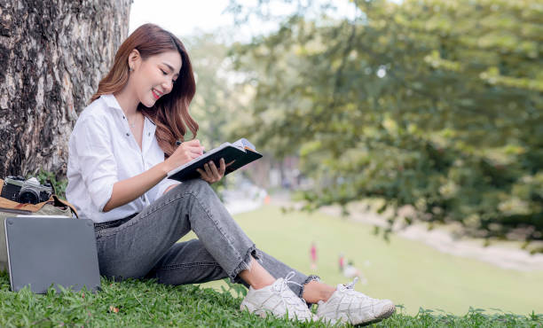 istock Female university student learning outdoor, sitting under big tree. 1351632801