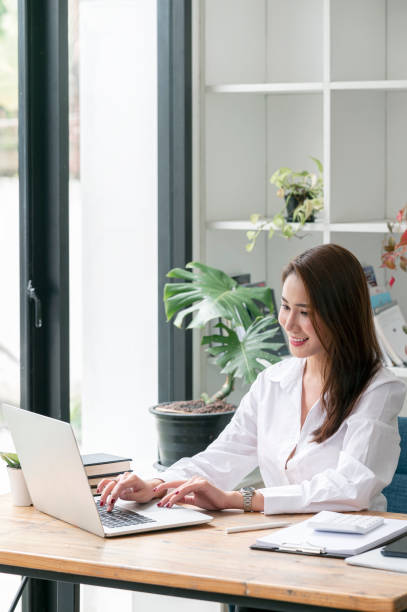 istock Beautiful asian woman working on laptop computer at office with happiness. Vertical view. 1351632830