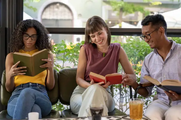 Photo of social and cultural inclusion in a literary cafeteria, group of young students read books and interact with each other having fun, focus on african woman face