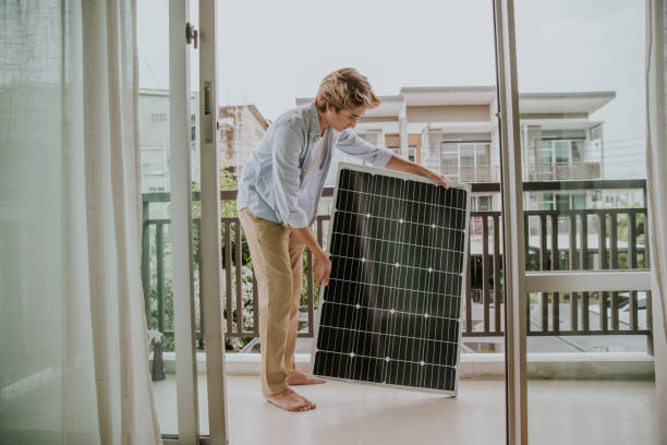 Southeast Asian gay person is setting a solar panel at home-stock photo Attractive gay man with an Alternative energy setting, he is preparing for setting a solar panel on the balcony. solar power station solar panel house solar energy stock pictures, royalty-free photos & images