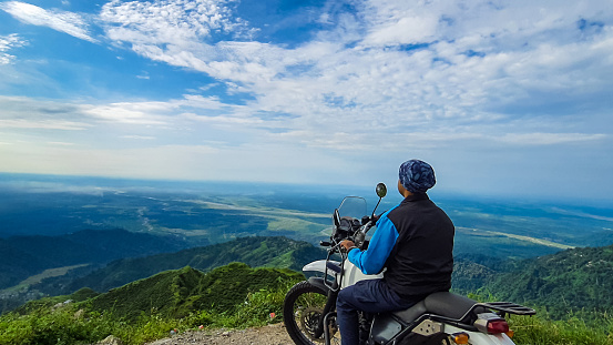 young man biker sitting on bike at mountain top with mesmerizing view at morning image is taken at kurseong darjeeling west bengal india.