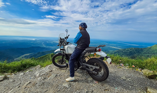 young man biker sitting on bike at mountain top with mesmerizing view at morning image is taken at kurseong darjeeling west bengal india.