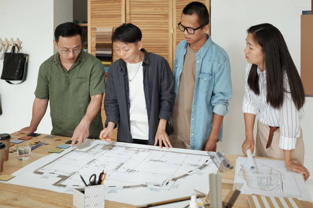 istock Group of young architects gathered by table with large sketch 1351641340