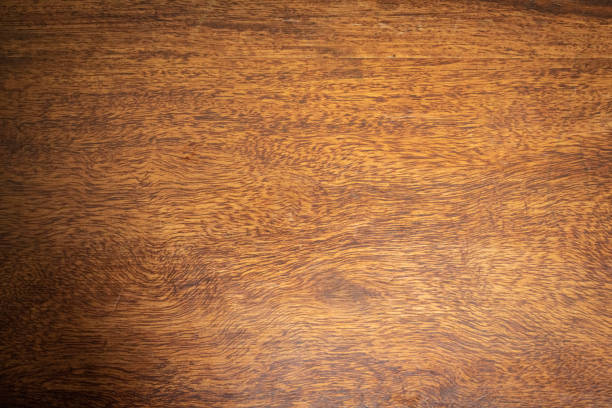 Weathered and scratched rustic wooden board.High angle view of a flat textured wooden board backgrounds. It has a beautiful nature and abstractive pattern. A close-up studio shooting shows details and lots of wood grain on the wood table. The piece of wood at the surface of the table also appears rich wooden material on it. The wood is dark brown color with darker brown lines and pattern on the bottom. Flat lay style. Its high-resolution textured quality.The close-up gives a direct view on the table, showing cracks and knotholes in the wood.