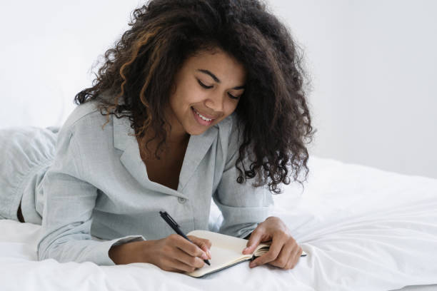 afro american woman writes down information in notebook - lying down women laptop freedom imagens e fotografias de stock