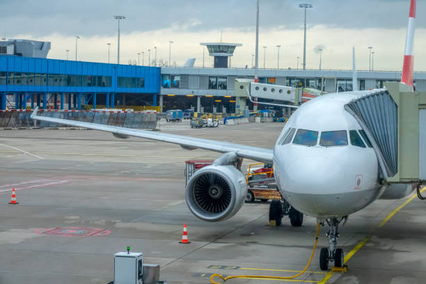 Airplane at the Airport With an Attached Jet Bridge for Passengers Cloudy day at the modern airport. The plane stands with an attached jet bridge for boarding and disembarking passengers voyager 1 stock pictures, royalty-free photos & images