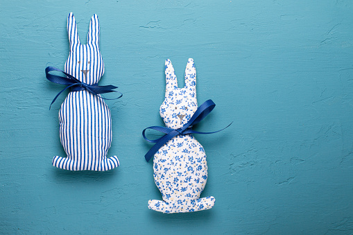 handmade toy bunnies on a blue slate, stone or concrete background. top view. a place to copy. the concept of needlework and sewing.