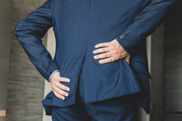 istock office worker holds his hand over his sore back. Health problems from sedentary work. Casual businessman touching his sore back in his office 1351647745