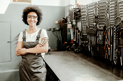 Portrait of young african american woman, professional female mechanic smiling at camera standing in auto repair shop