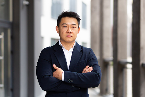 portrait of a serious asian in a business suit looking at the camera with arms crossed
