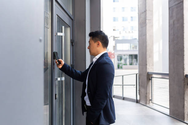 exitoso empresario asiático abre la puerta del centro de oficinas utilizando un smartphone y una aplicación nfc - alcanzable fotografías e imágenes de stock