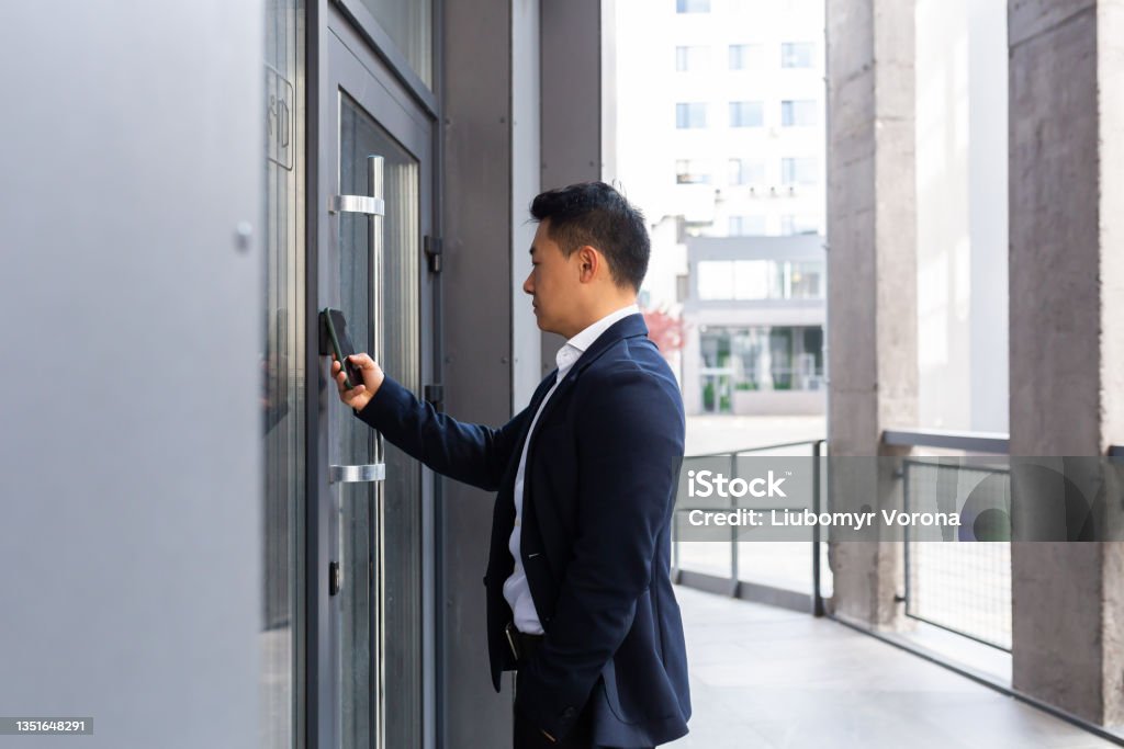 Successful Asian businessman opens the door of the office center using a smartphone and NFC application Accessibility Stock Photo