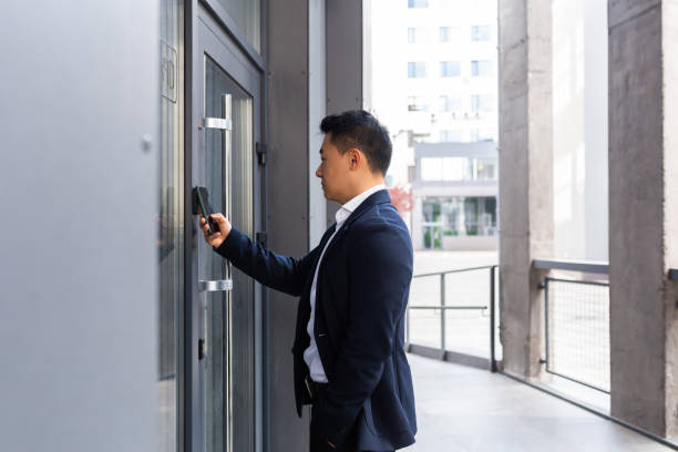 Successful Asian businessman opens the door of the office center using a smartphone and NFC application Successful Asian businessman opens the door of the office center using a smartphone and NFC application control stock pictures, royalty-free photos & images