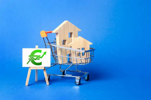 Photo of Houses in a shopping cart and an easel with euro green up arrow. Market growth, attracting investment. Raising taxes and house maintenance. Real estate price increases. High demand and value.