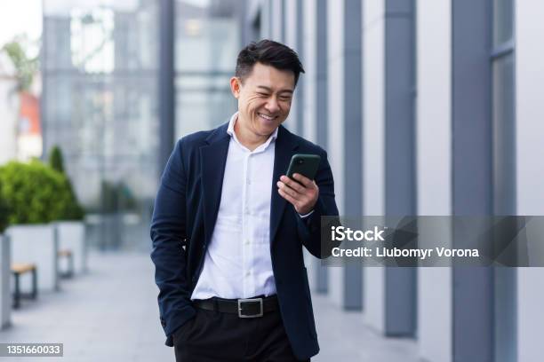 Asian Male Freelancer Walking Near Business Center Holding Phone Smiling Reading News Successful Businessman Stock Photo - Download Image Now