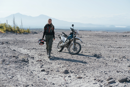 Woman motorcyclist in area of active volcano Shiveluch.  Dry river desert. Post-apocalyptic landscape, Kamchatka
