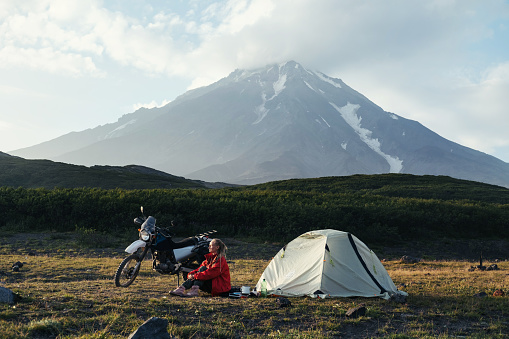 woman traveling on a motorcycle sitting near a tent under the active volcano Koryaksky, Kamchatka