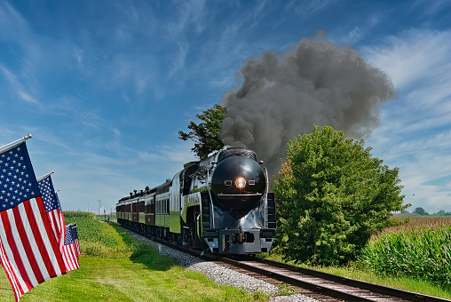 A Antique Restored Steam Engine Approaching Head on Passing a Row of American Flags on a Beautiful Sunny Day