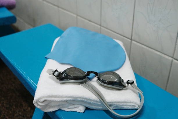 Things for the pool - a towel, a rubber cap and swimming goggles lying on a blue bench.