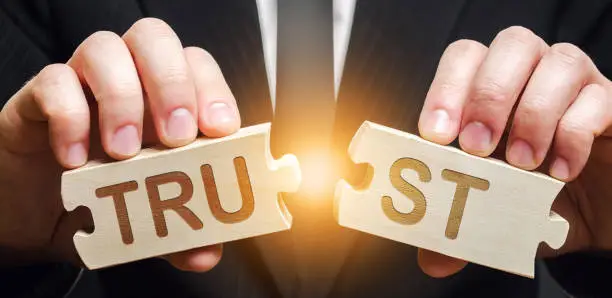 Photo of A man shares two puzzles with the word Trust. Violation of agreements and promises. Lose credibility. Failed to maintain professional reputation. Lie and cheat. Bad consequences. Not trustworthy