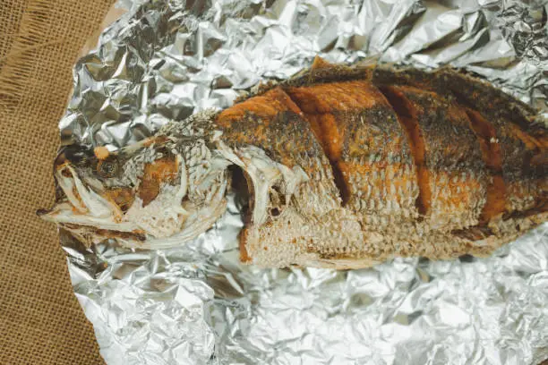 Photo of Fried sea bass fish in foil paper in Thai style. Top view