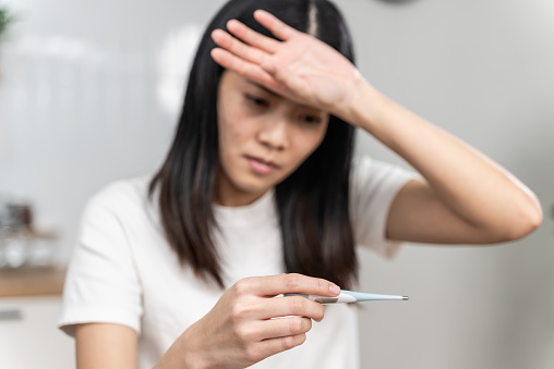 Close-up woman hand holding thermometer, Sick young Asian woman looking at thermometer and touching her forehead.