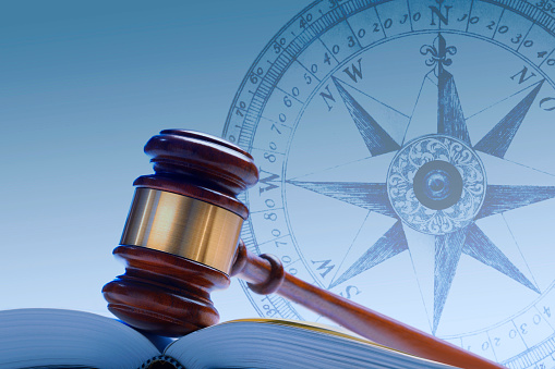 A gavel rests in the fold of an open law book in front of a compass.