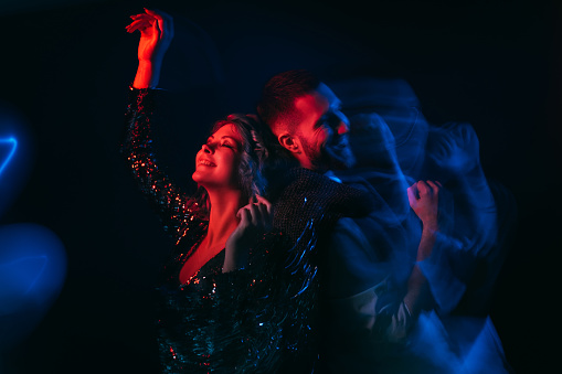 Party joy. Celebrating couple. Christmas inspiration. Happy man and woman feeling excitement enjoying dance long exposure red blue neon light motion blur isolated black.