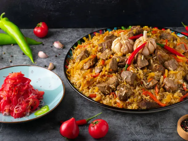 Uzbek pilaf and ingredients on black wooden background. Plov - rice prepared with vegetables and meat.