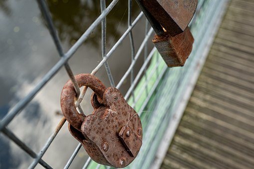 Shallow focus of old and heavily rusted padlocks seen attached to a river bridge's barrier. It is one of many padlocks on the barrier.