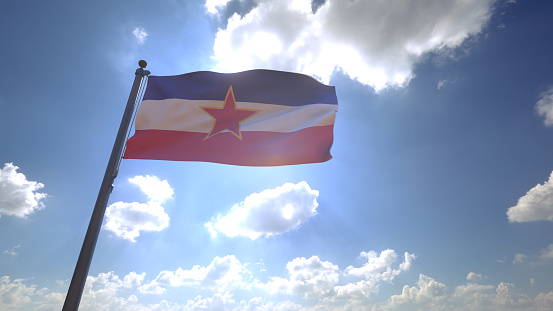 Bandera de Yugoslavia en un poste con cielo azul y nubes al fondo photo