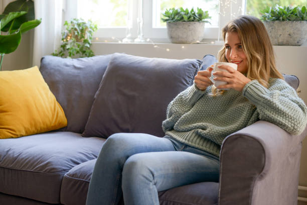 istock attractive middle aged woman sitting on the couch (drinking hot tea) 1351703286
