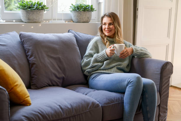 istock attractive middle aged woman sitting on the couch (drinking hot tea) 1351704109