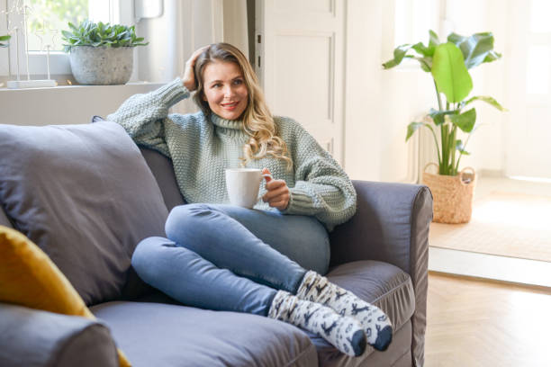 istock attractive middle aged woman sitting on the couch (drinking hot tea) 1351704295