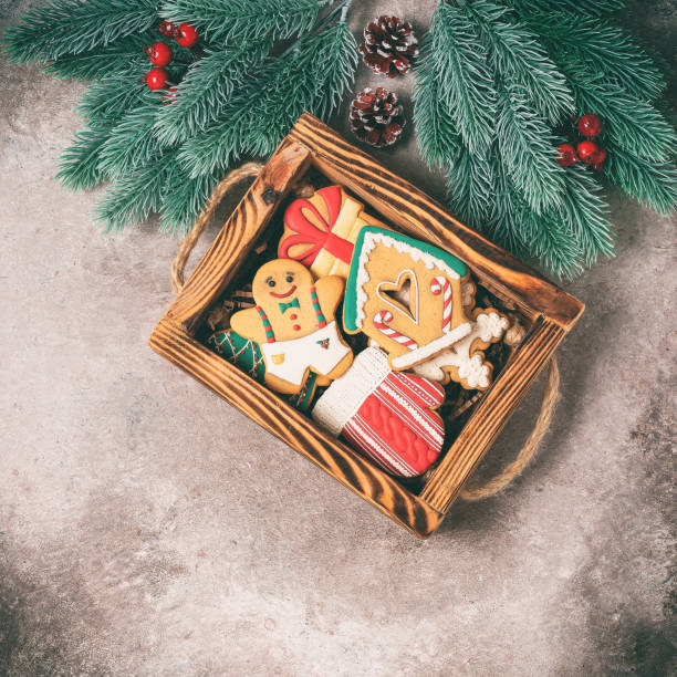 Christmas gingerbread cookies on a wooden tray decorated with fir branches with holly and cones. Dark brown rustic background. Top view, flat lay. Toned photo