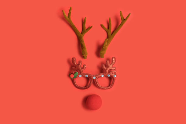 funny christmas face with antlers of a deer, toy glasses and a clown nose on a red background - clowns nose imagens e fotografias de stock